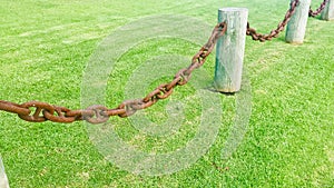 A brown rusty chains with pole and green lawn.