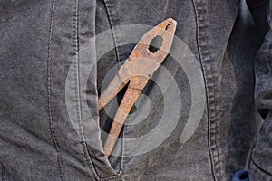 brown rusty old iron pliers lies in a gray jacket pocket