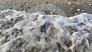 Brown sand beach and the foam of the waves hitting the small white pebbles