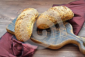 Brown sandwich bun with seeds on brown cutting board with napkin of grenadine color