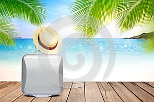 Brown straw hat and suitcase on wooden table with blurred sea,blue sky and palm tree background with copy space.