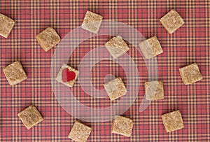 Brown sugar cubes with a red heart on one of them. Top view. Diet unhealty sweet addiction concept photo