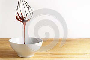 Brown sugar syrup flows from a wire whisk into a white bowl, wooden table and bright background with large copy space