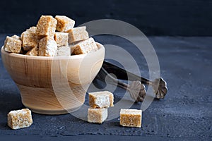 Brown sugar in a wooden bowl on a dark background, copy space