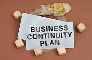 On a brown surface are coins, cubes and a business card with the inscription - Business Continuity Plan