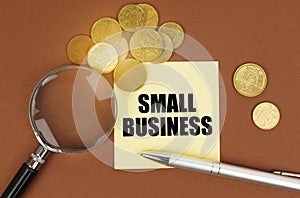 On a brown surface are coins, a pen, a magnifying glass and stickers with the inscription - Small business