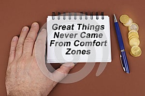 On a brown surface are coins, a pen and a notepad with the inscription - Great Things Never Came From Comfort Zones