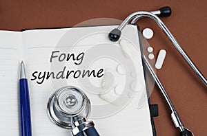 On a brown surface lie pills, a pen, a stethoscope and a notebook with the inscription - Fong syndrome