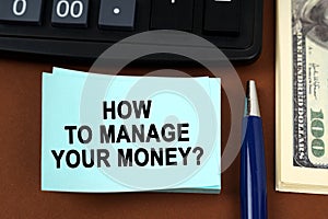 On a brown surface lies a calculator, dollars, pens and stickers with the inscription - How to manage your money