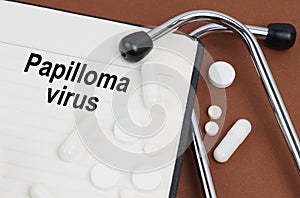 On a brown surface lies a stethoscope, pills and a notepad with the inscription - Papilloma Virus
