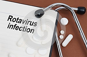 On a brown surface lies a stethoscope, pills and a notepad with the inscription - Rotavirus infection
