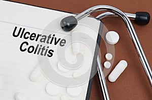 On a brown surface lies a stethoscope, pills and a notepad with the inscription - Ulcerative Colitis