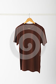Brown t shirt on hanger hanging from clothes rail with copy space on white background