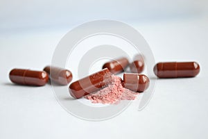 Brown tablets, gelatin capsules, one of them is open and with the poured pink powder with gray backdround