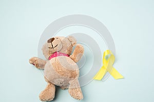 Brown teddy bear holds in his paw a yellow ribbon folded in a loop on a blue background