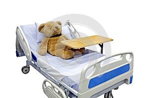 Brown teddy bear lying sick in bed with overbed table on body