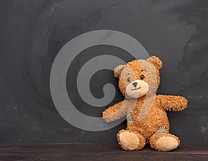 Brown teddy bear sits on a brown wooden table, behind an empty black chalk board