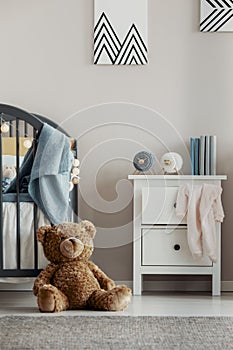 Brown teddy bear on the wooden floor of scandinavian baby bedroom interior