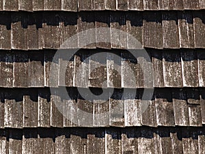 Brown texture of wooden tile roof. Shingle aged wooden Background. Backdrop with small overlapping colored wooden shingles on roof