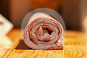 Brown three-ply microfibre tea towel rolled up on a wooden surface