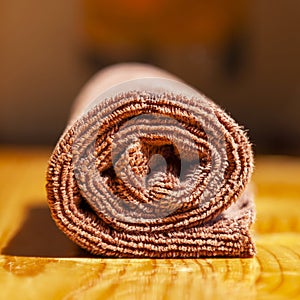 Brown three-ply microfibre tea towel rolled up on a wooden surface