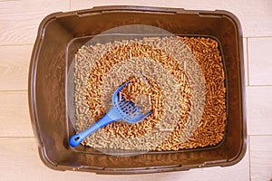 Brown toilet tray for cat with wood pellets and scoop. The cats toilet clean is filled with granules of wood. Wooden filler for