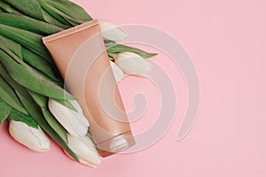 Brown tube with cosmetic cream or lotion for body and bouquet of white tulips, pink background, copy space