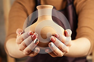 Brown vase from clay in the potter`s hands close up. a young and cheerful woman holding a vase of clay. The potter works