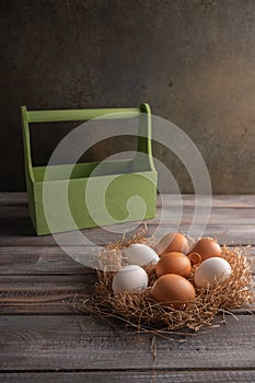 Brown and white chicken eggs in a straw nest on wooden background. Behind a wooden box. Space under your text