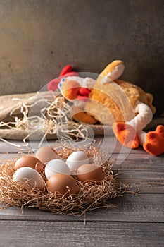 Brown and white chicken eggs in a straw nest on wooden background. Next to a chicken toy sleeping. Vertical orientation