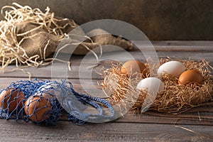 Brown and white chicken eggs in a straw nest on wooden background. Next to eco string bag with eggs. Rustic style