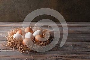 Brown and white chicken eggs in a straw nest on wooden background. Rustic style