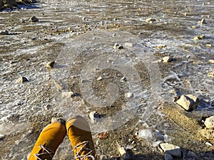 Brown winter hiking shoes on frozen sheet of ice forming on surf