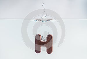 Brown wooden alphabet H drop in the water with white background and selective focus