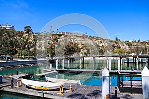 A brown wooden dock with boats parked at the dock, a long brown wooden pier surrounded by a cliff with beach front homes on top