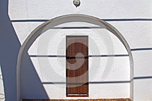 Brown wooden door in the arc on the white wall. Summer, Spain