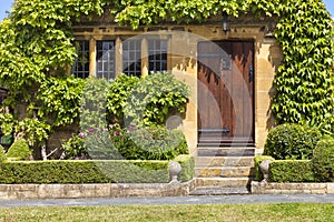 Brown wooden doors to traditional English stoned cottage, garden