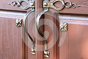 Brown wooden entrance door with gold-plated forged handles and ornate outside.