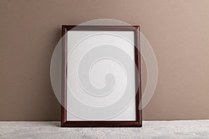 Brown wooden frame mockup on beige paper background. Blank, vertical orientation, still life