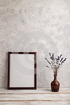 Brown wooden frame mockup with lavender in ceramic vase on gray concrete background. Blank, vertical orientation, copy space