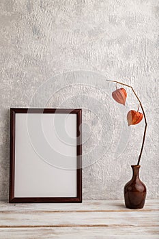 Brown wooden frame mockup with physalis in ceramic vase on gray concrete background. Blank, vertical orientation, copy space