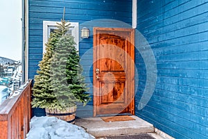 Brown wooden front door and Christmas tree at the facade of vibrant blue home