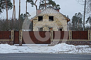 Brown wooden gate and fence in front of an unfinished home on the asphalt road in the snow