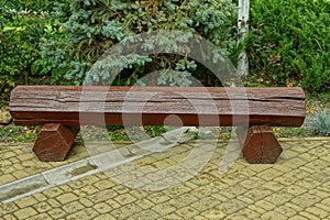 A brown wooden log bench stands on a gray sidewalk