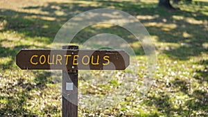 Brown wooden sign in grassy field with courteous written on it