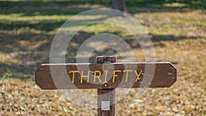 Brown wooden sign in grassy field with thrifty written on it