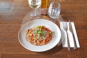 Brown wooden table and White plate with ragu sauce on Linguine