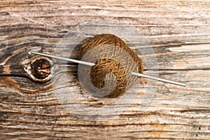 Brown wool spool and a crochet needle on a wooden background