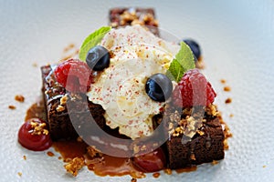 Brownie cake with salted caramel. Anglaise foam, raspberry sauce, praline nut and fresh berry. Delicious sweet dessert