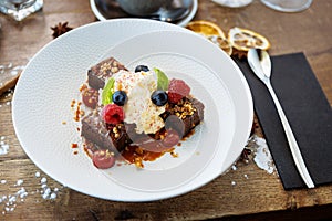 Brownie cake with salted caramel. Anglaise foam, raspberry sauce, praline nut and fresh berry. Delicious sweet dessert